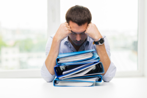 business, people, deadline, stress and paperwork concept - sad businessman with stack of folders at office